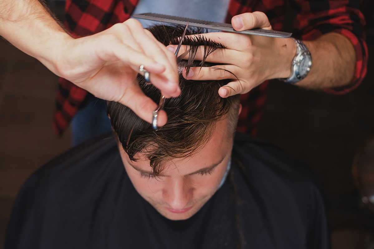 Caucasian young man in Barbershop. Barber is cutting his hair in hipster style. Hair care concept