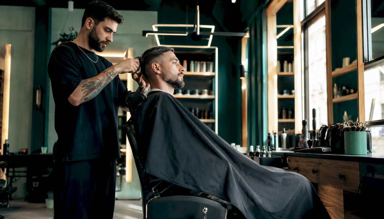 Štýlový pánsky barbershop s moderným interiérom, kde práve holič upravuje vlasy zákazníkovi.