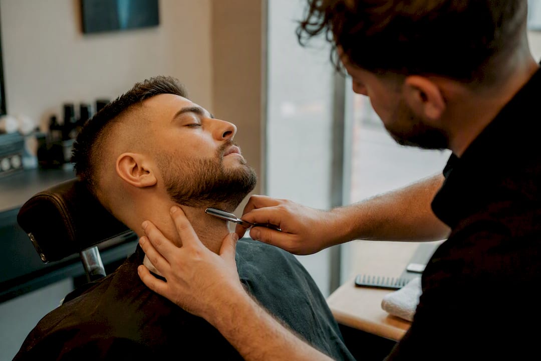 Barber upravuje kontúry brady, aby vyzerala dokonale a upravene.